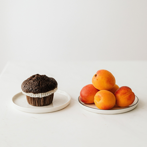 Two plates of food, one with a chocolate muffin and one with a pile of apricots