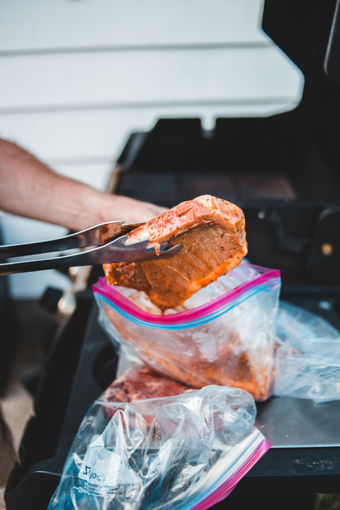 Person pulling marinated steak from a prepped bag with a pair of tongs.