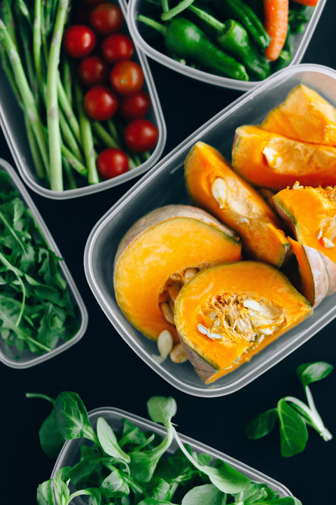 Fresh prepped vegetables in plastic containers, including, squash, cherry tomatoes, asparagus, peppers, carrots, and lettuce.