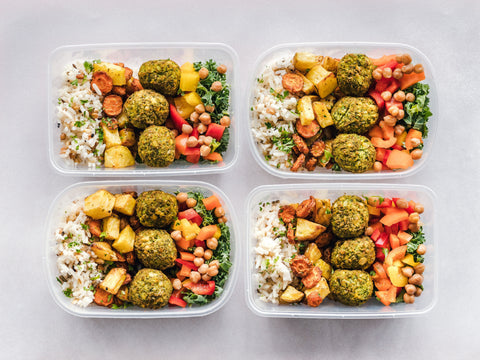 Four prepped mediterranean meals, with rice, potatoes, falafel, tomatoes, chickpeas, and greens.