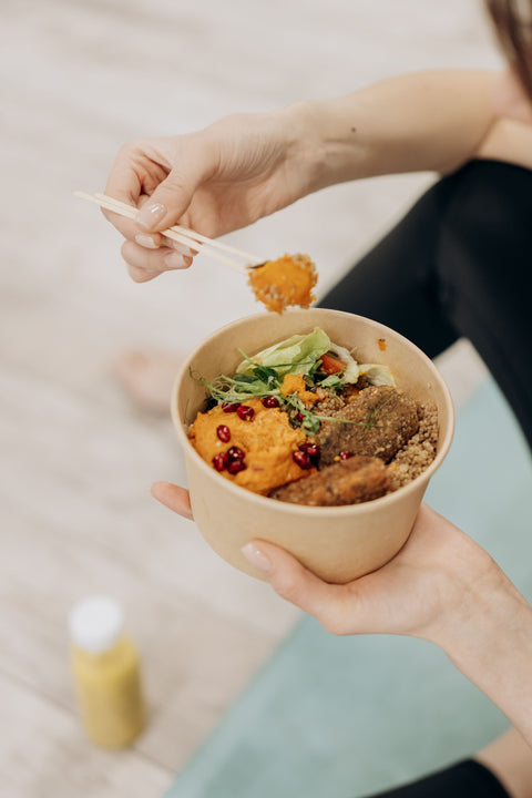 Person sitting on a yoga mat, eating a bowl of healthy foods and drinking a fresh juice.