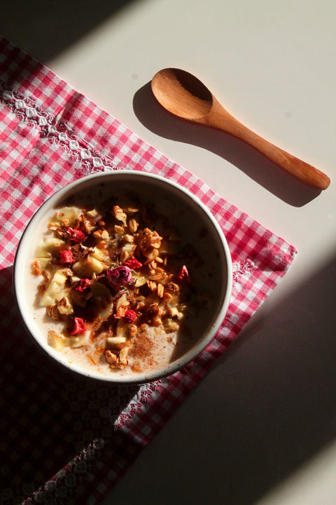 Prepared bowl of overnight oats covered in strawberries, cinnamon, and nuts, sitting on a checkerboard tablecloth next to a wooden spoon.