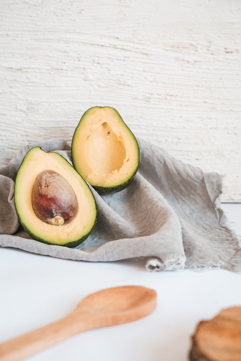 Sliced avocado sitting on a dishtowel on a countertop, resting against a wall, with a wooden spoon resting nearby.