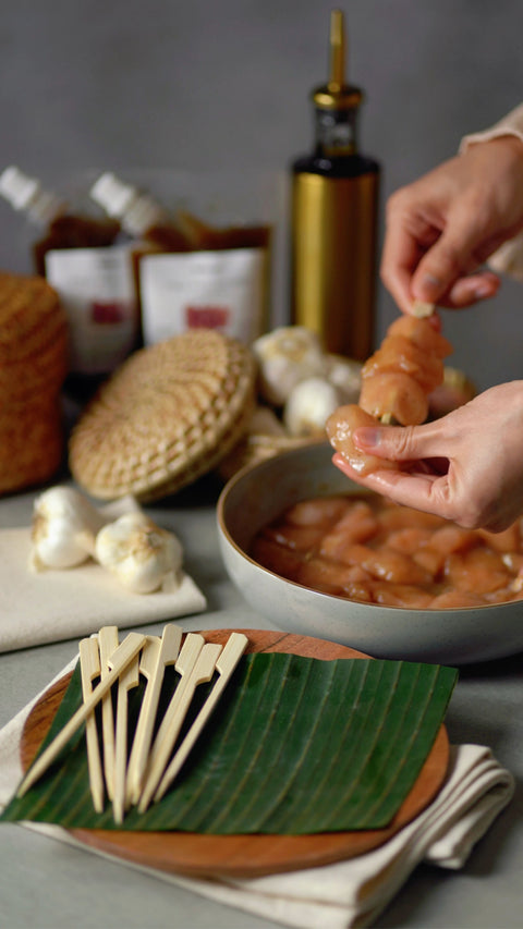 Person putting chicken on skewers, with kitchen countertop backdrop.