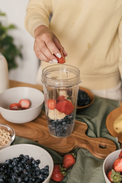 Person prepping a smoothie, putting strawberries, blueberries, and bananas into a blender.