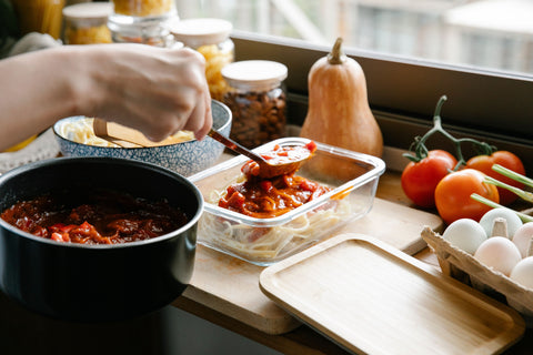 Person meal prepping spaghetti, with a kitchen countertop backdrop.