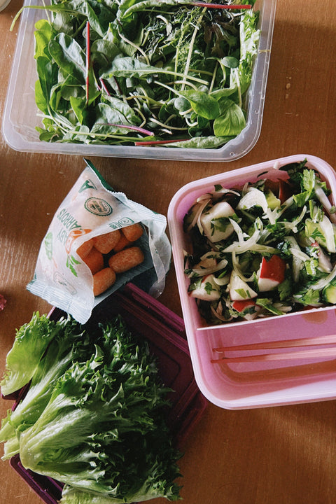 Two containers of prepped salads on a cutting board, with a small package of croutons and a handful of fresh lettuce.