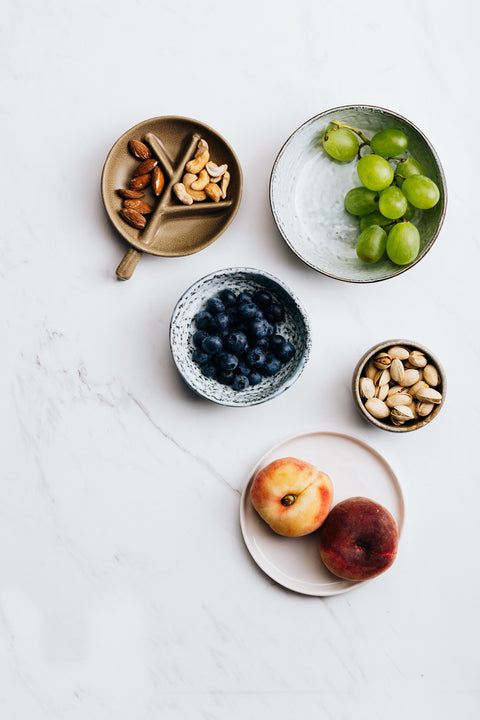 Five plates of food on a countertop, filled with various fruits and nuts. 